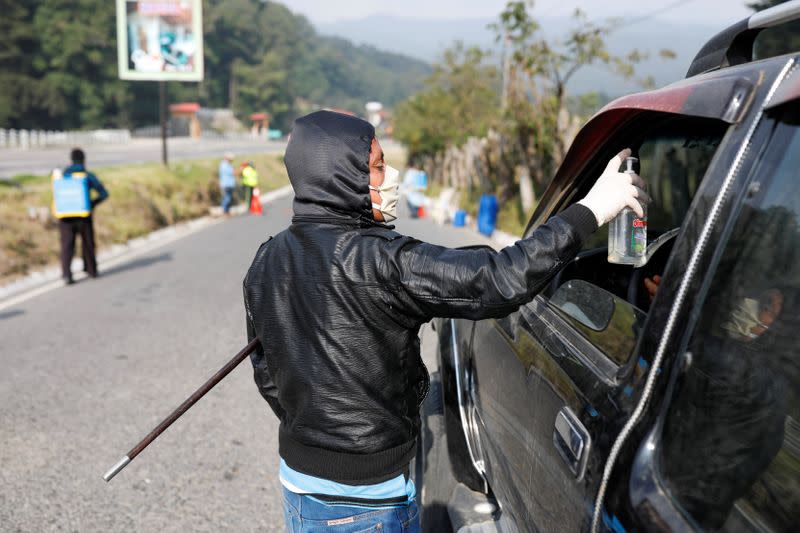 A community member working a checkpoint at the entrance to the village of Tecpan administers disinfectant to a driver amid the outbreak of the coronavirus disease (COVID-19), in Chimaltenango