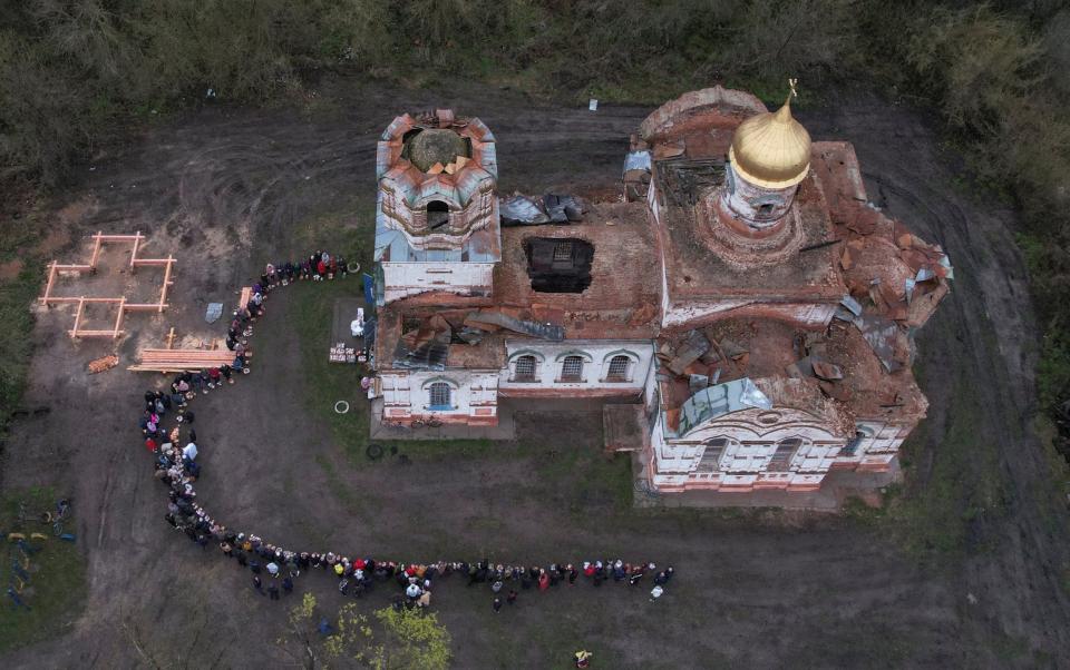 An Orthodox priest sprays holy water on believers during the celebration of Orthodox Easter in front of a heavily damaged church - VALENTYN OGIRENKO/REUTERS