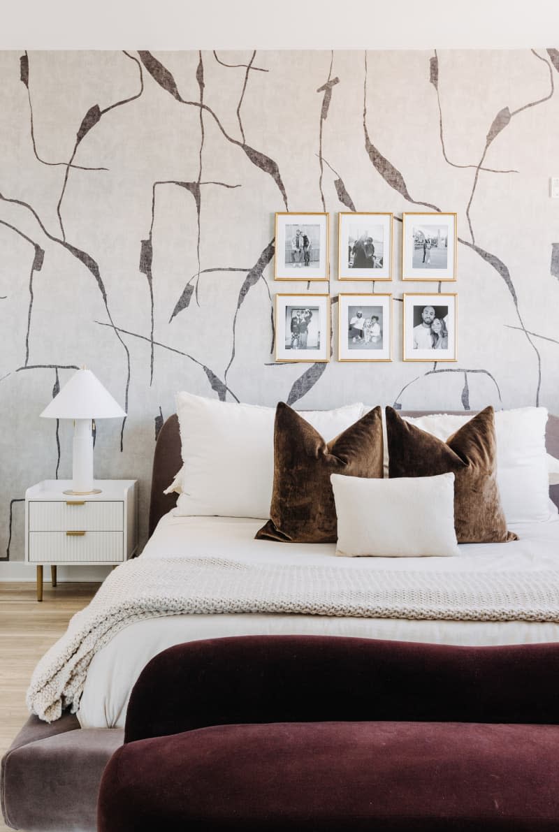 White bedroom with one gray and white patterned wallpaper wall, gray velvet bed, and other velvet accents