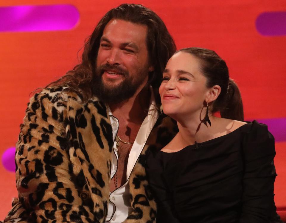 Jason wears a leopard jacket while sitting next to Emilia during a talk show interview