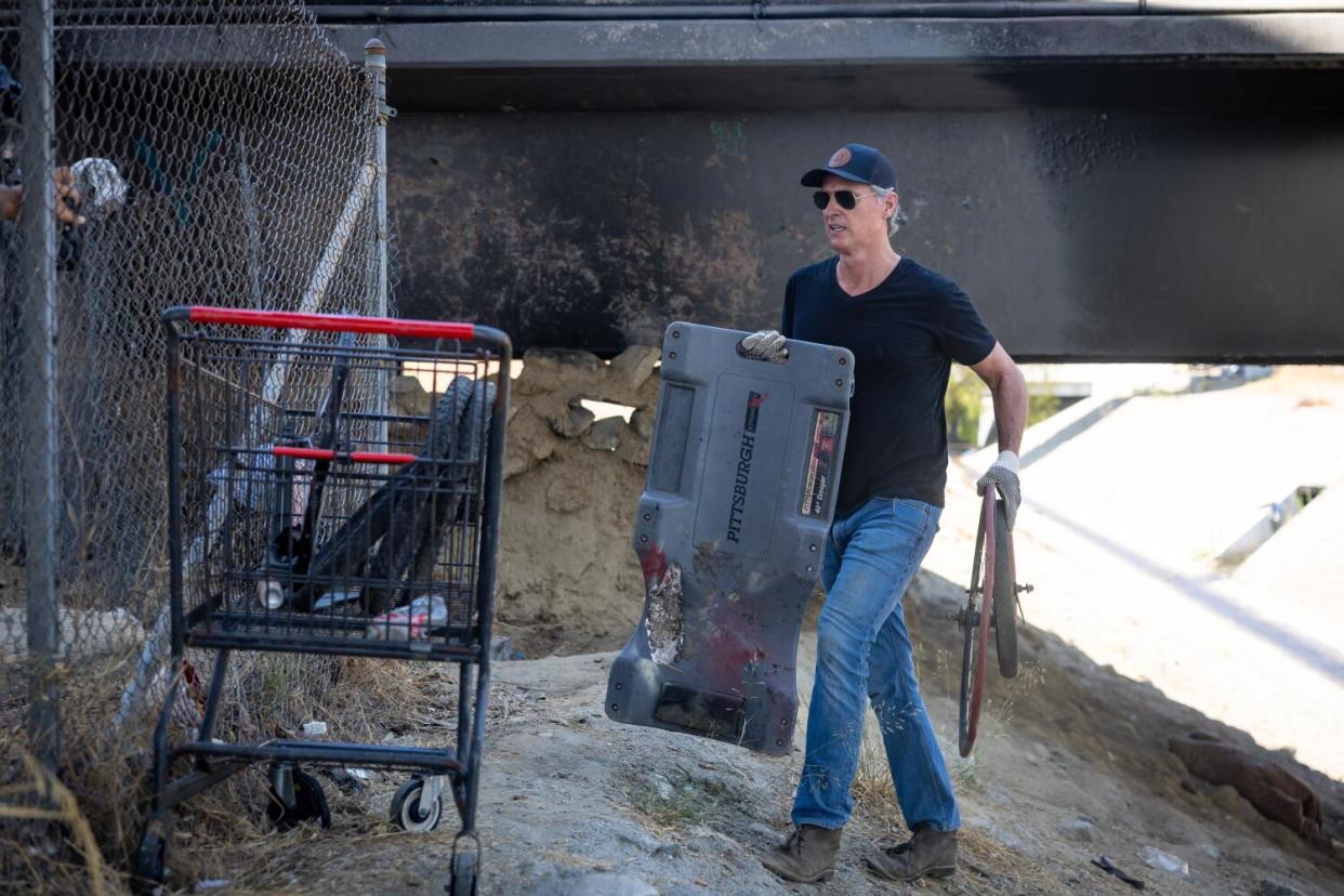 A man carries a large rectangular object past an abandoned shopping cart.