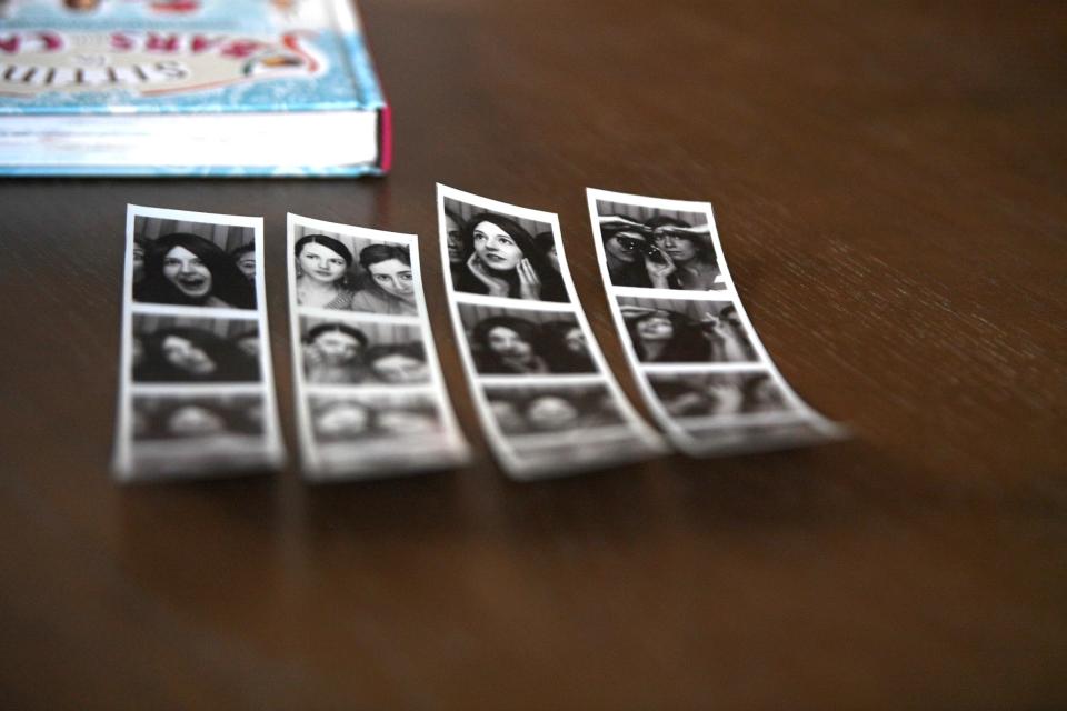 Photo booth strips of Audrey Shulman and Chrissy Osmulski from the 2010s next to Shulman's 2015 book “Sitting in Bars with Cake” at Shulman's home in Nashville, Tenn., Dec. 6, 2023.