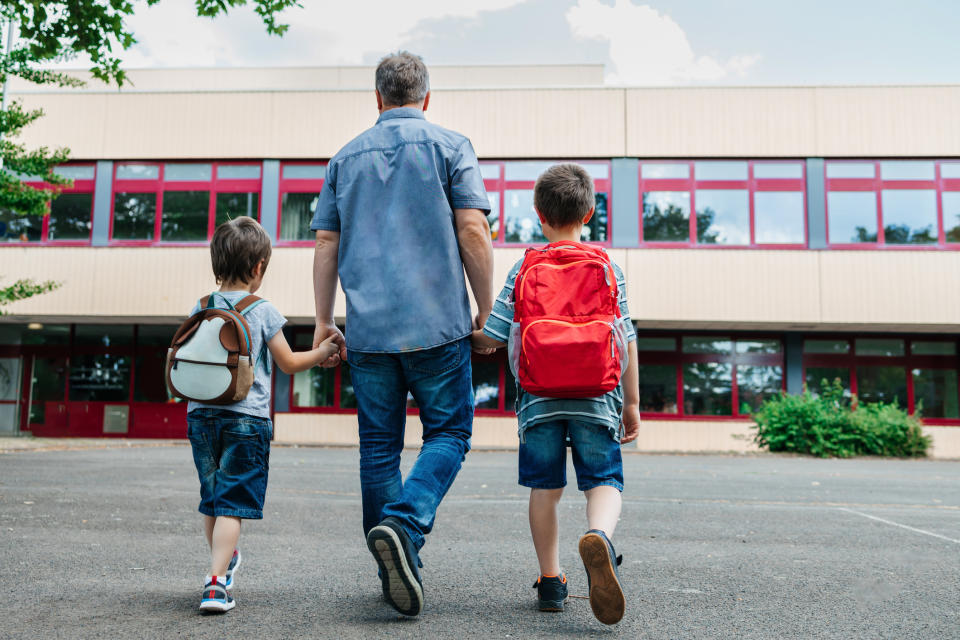 Man walks with two children carrying backpacks towards a school building