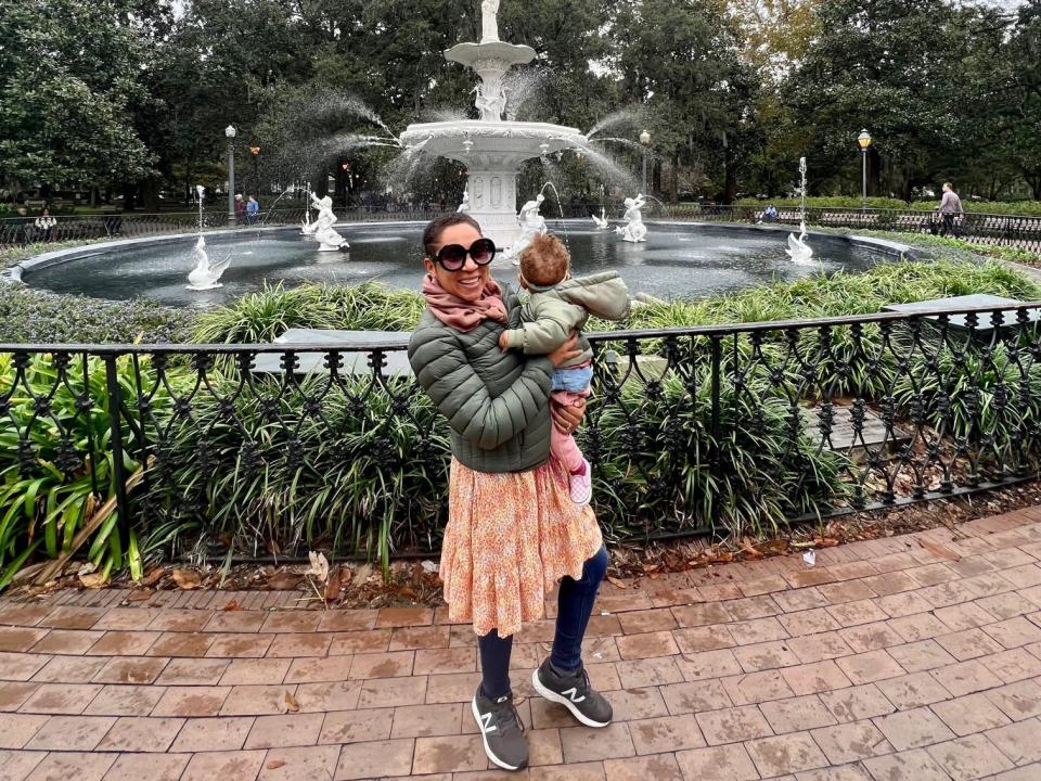 Stephanie Claytor holding her child and smiling in front of a fountain.