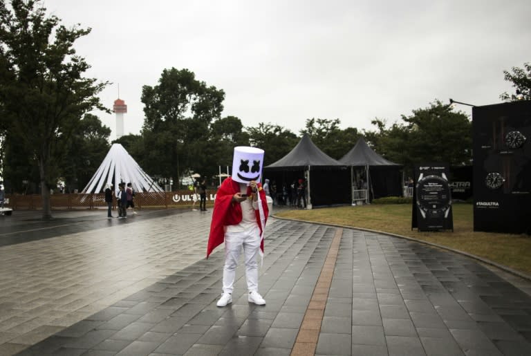 A Japanese man wearing a mask checks his mobile phone as he attends the Japan Ultra Music Festival at Odaiba Ultra Park in Tokyo