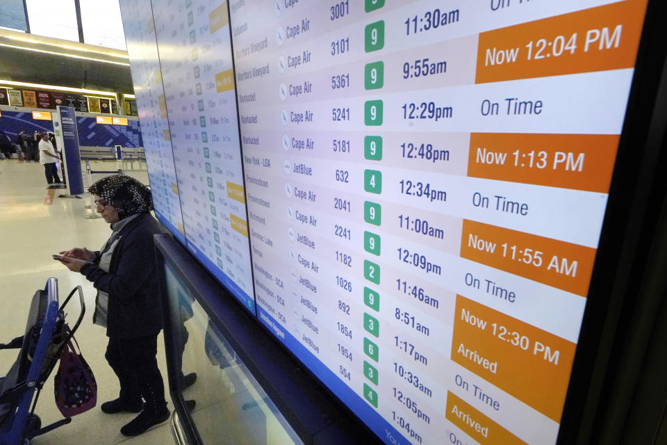 A woman views her phone near a flight board at Boston Logan International Airport, Wednesday, June 28, 2023, in Boston. Travelers are getting hit with delays at U.S. airports again early Wednesday, an ominous sign heading into the long July 4 holiday weekend. (AP Photo/Steven Senne)