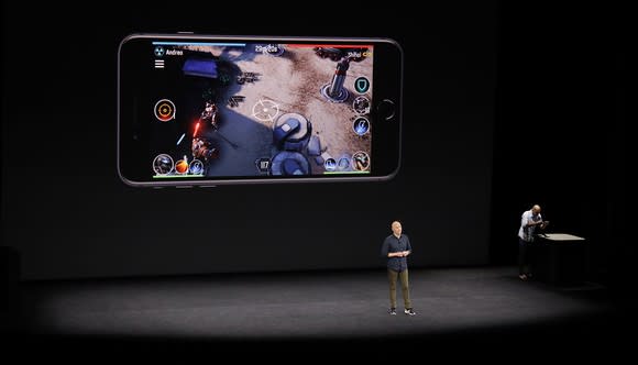 A person on stage with an iPhone playing a 3D game projected on the screen behind him.