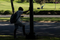 A boy waits for a shuttle as a man golfs at the Ka'anapali Golf Courses, Wednesday, Dec. 6, 2023, in the beach resort community of Kaanapali in Lahaina, Hawaii. Residents and survivors still dealing with the aftermath of the August wildfires in Lahaina have mixed feelings as tourists begin to return to the west side of Maui. (AP Photo/Lindsey Wasson)
