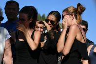 People react as they stand next to the make-shift memorial where people laid flowers to pay tribute to the victims of the truck attack in Nice on July 15, 2016