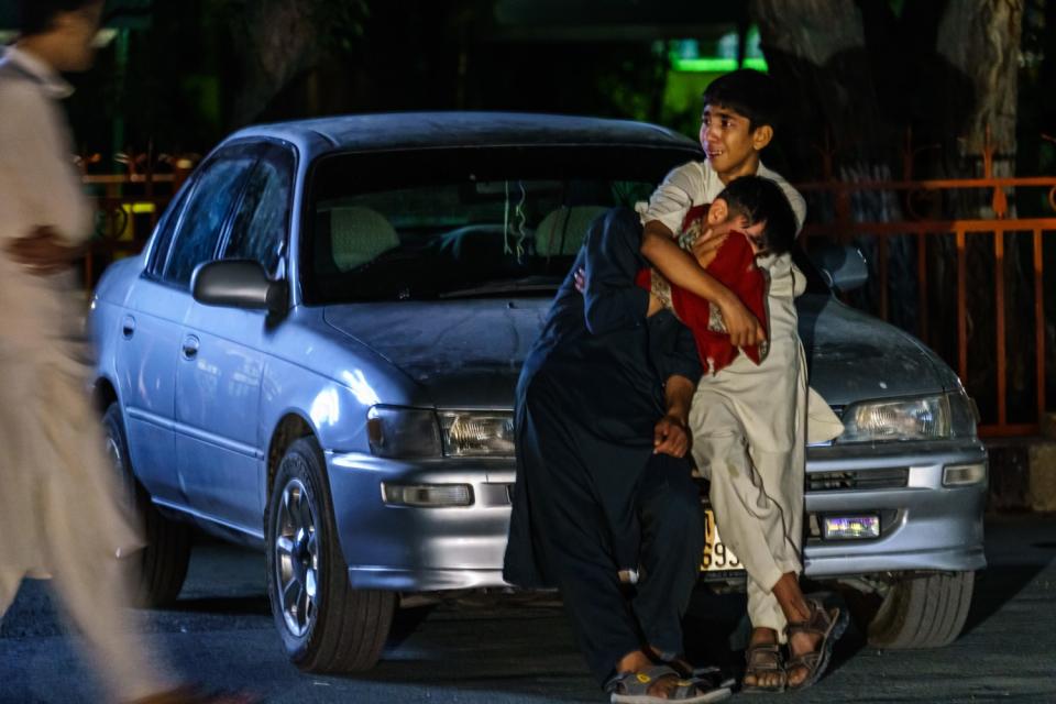 Two boys embrace each other next to a car