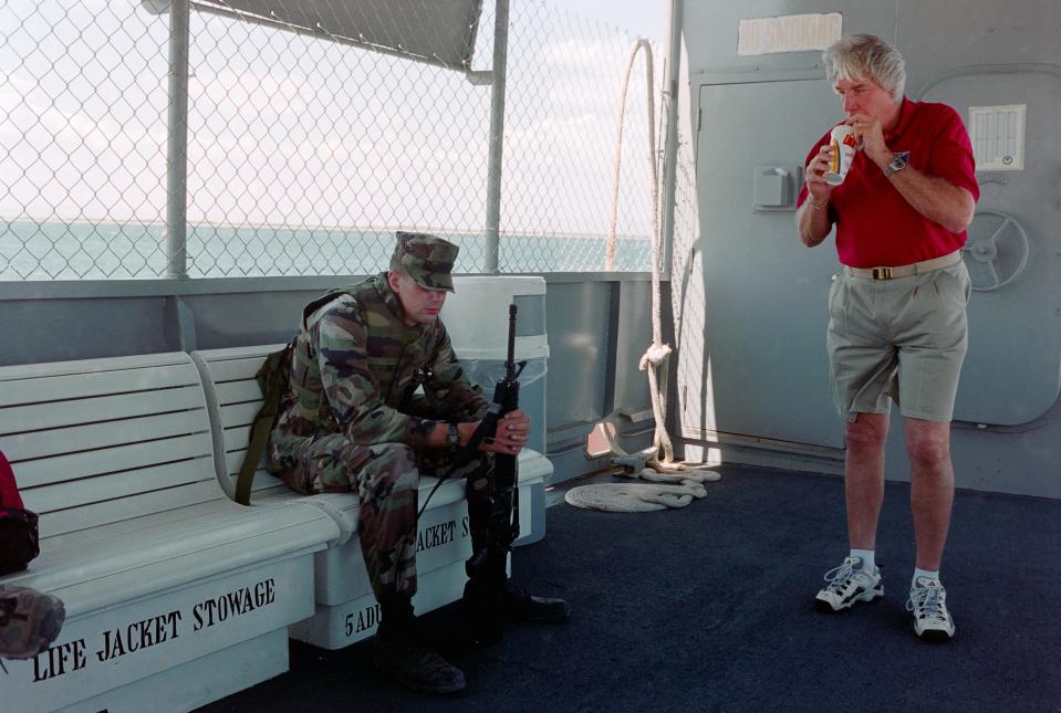 A man sips from a straw while a soldier sits nearby.