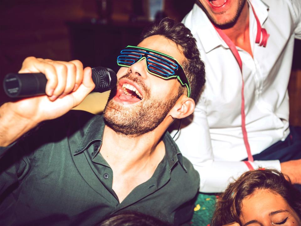 Close-up of young man singing karaoke while enjoying with friends in party.