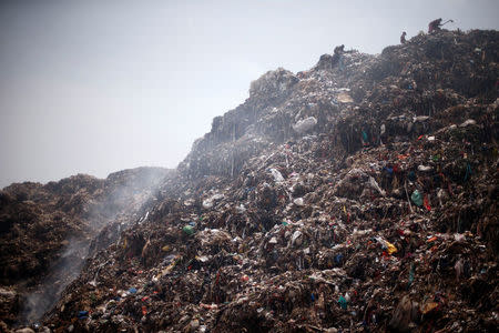 People collect recyclable materials as smoke billows from a burning garbage dump site in New Delhi, May 2, 2018. REUTERS/Adnan Abidi