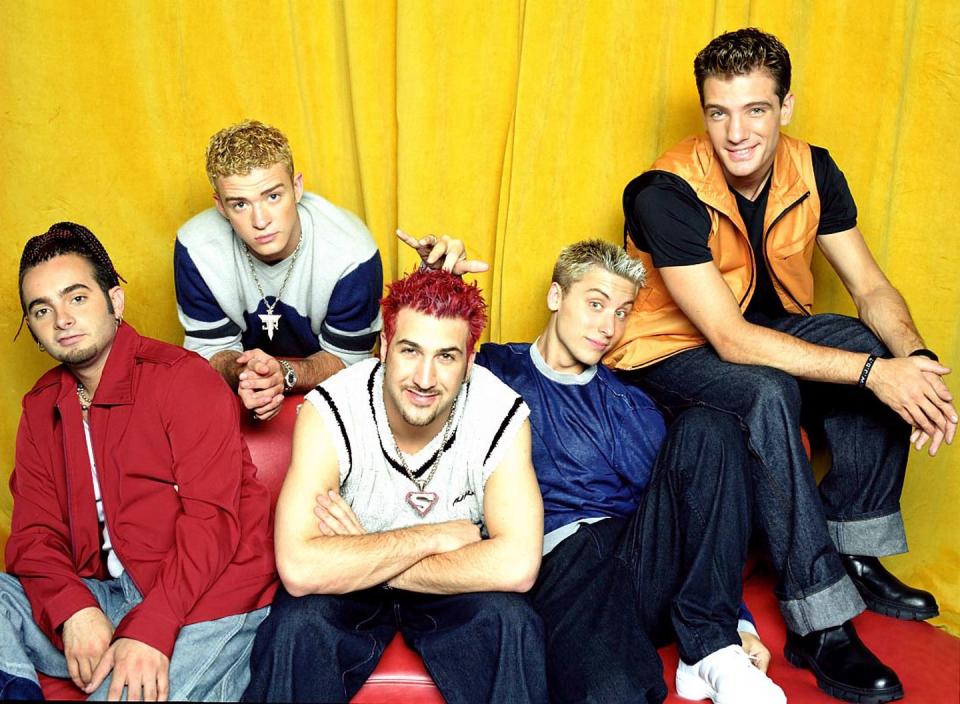 chris kirkpatrick, justin timberlake, joey fatone, lance bass, and jc chasez pose for a photo while sitting in front of a yellow background