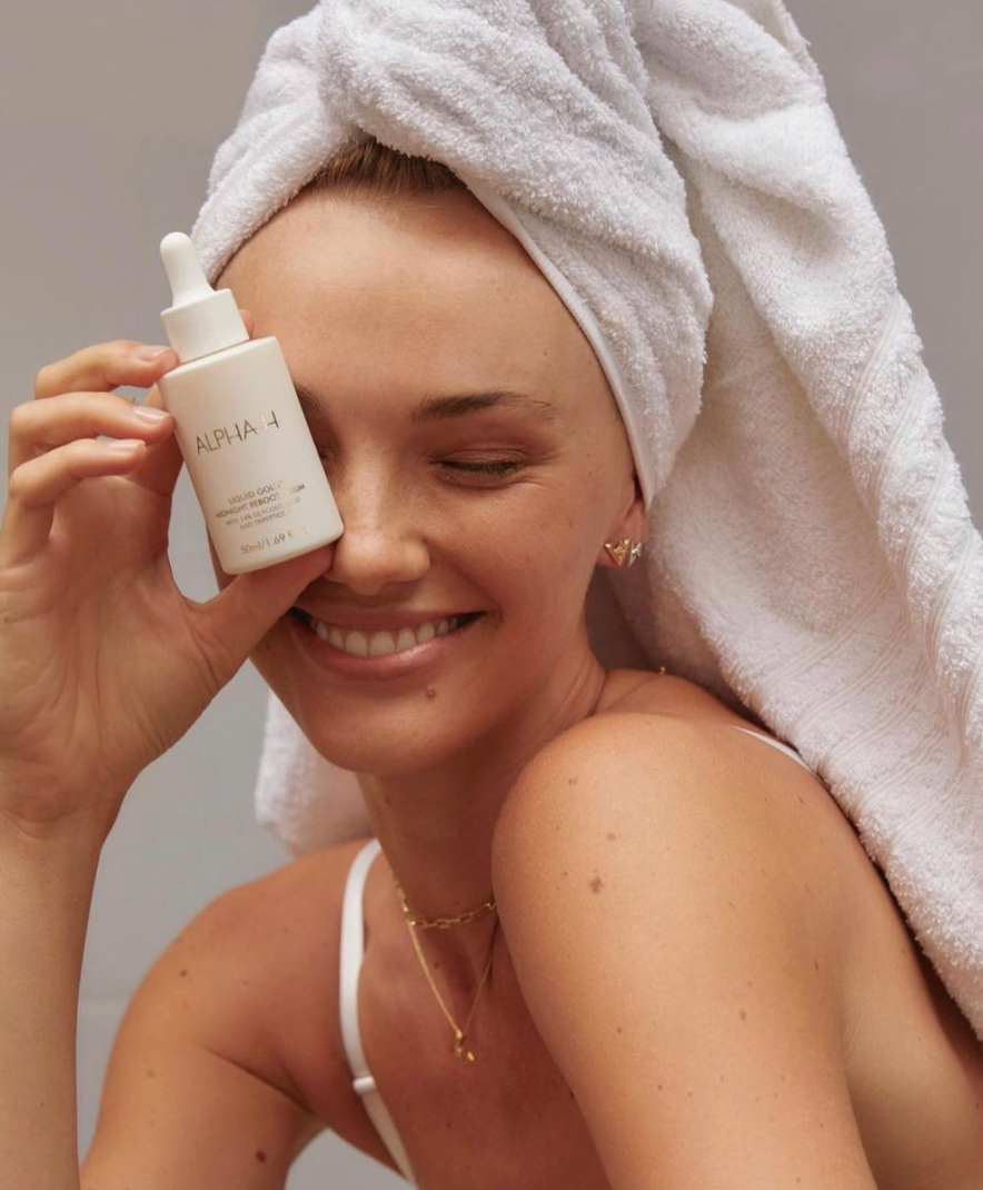 Woman with a towel wrapped around her head holding female-founded Aussie beauty brand Alpha-H's liquid gold product 