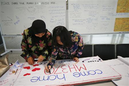 Women put the final touches to a sign of support and hope for the passengers of the missing Malaysia Airlines flight MH370 they made and brought to the Kuala Lumpur International Airport March 11, 2014. REUTERS/Damir Sagolj