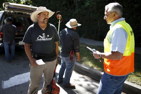 Department of Water and Power (DWP) Water Conservation Response Unit supervisor Enrique Silva (R) advises gardeners who were working at a home that had sprinklers operating on the wrong day of the week, as he patrols the streets looking for people wasting water during the drought in Los Angeles, California, April 17, 2015. REUTERS/Lucy Nicholson