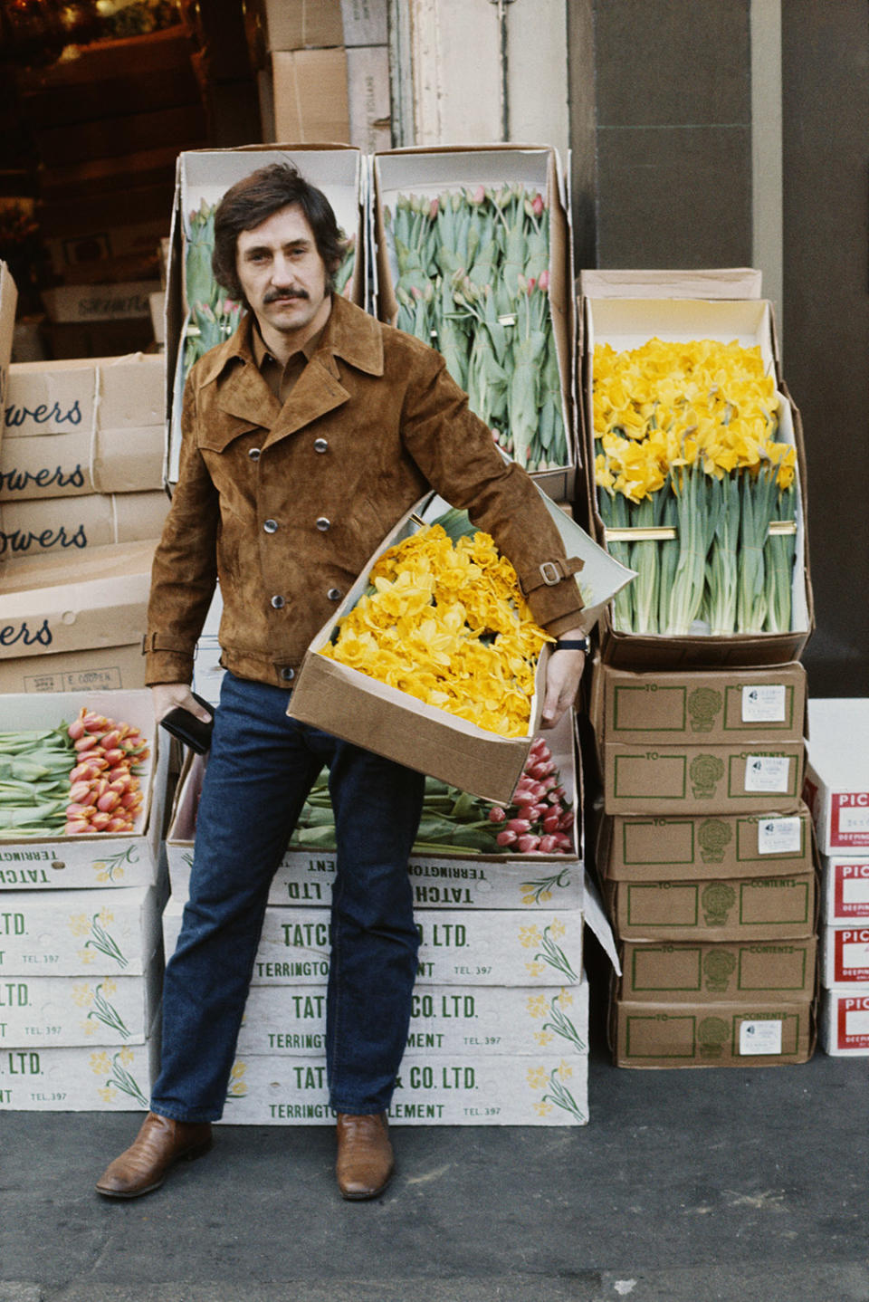 American pop artist Ed Ruscha holding a box of daffodils outside a florist's shop, circa 1970.