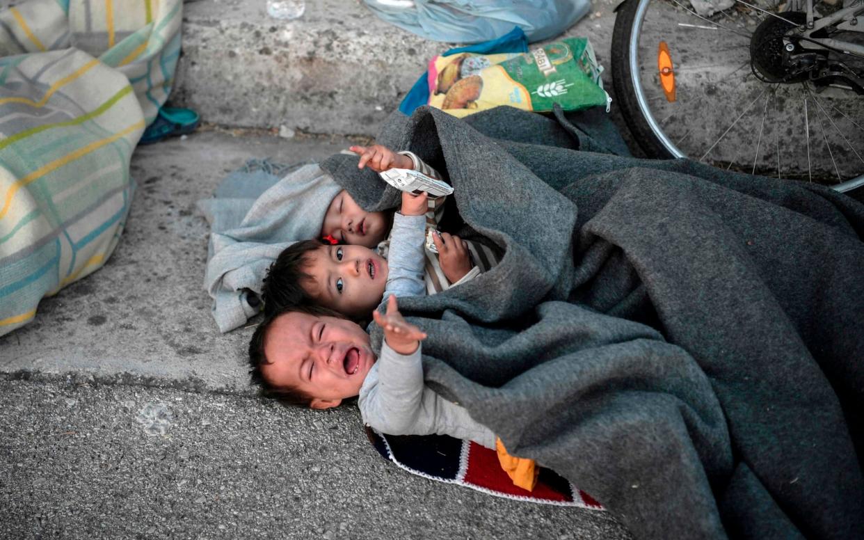 Children wake up after spending the night on the road near Mytilene after a fire destroyed Greece's largest Moria refugee camp on the island of Lesbos, early on September 10, 2020. - Greek authorities on September 10 were racing to shelter thousands of asylum seekers left homeless on Lesbos after the island's main migrant camp was gutted by back-to-back fires, which destroyed the official part of the camp housing 4,000 people. Another 8,000 lived in tents and makeshift shacks around the perimeter and many were badly damaged. (Photo by LOUISA GOULIAMAKI / AFP) (Photo by LOUISA GOULIAMAKI/AFP via Getty Images) - LOUISA GOULIAMAKI/AFP