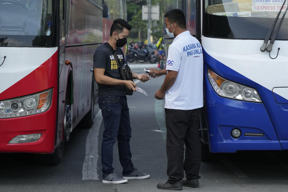 A man checks the temperature and vaccination card of a passenger before boarding a bus in Quezon city, Philippines on Monday, Jan. 17, 2022. People who are not fully vaccinated against COVID-19 were banned from riding public transport in the Philippine capital region Monday in a desperate move that has sparked protests from labor and human rights groups. (AP Photo/Aaron Favila)