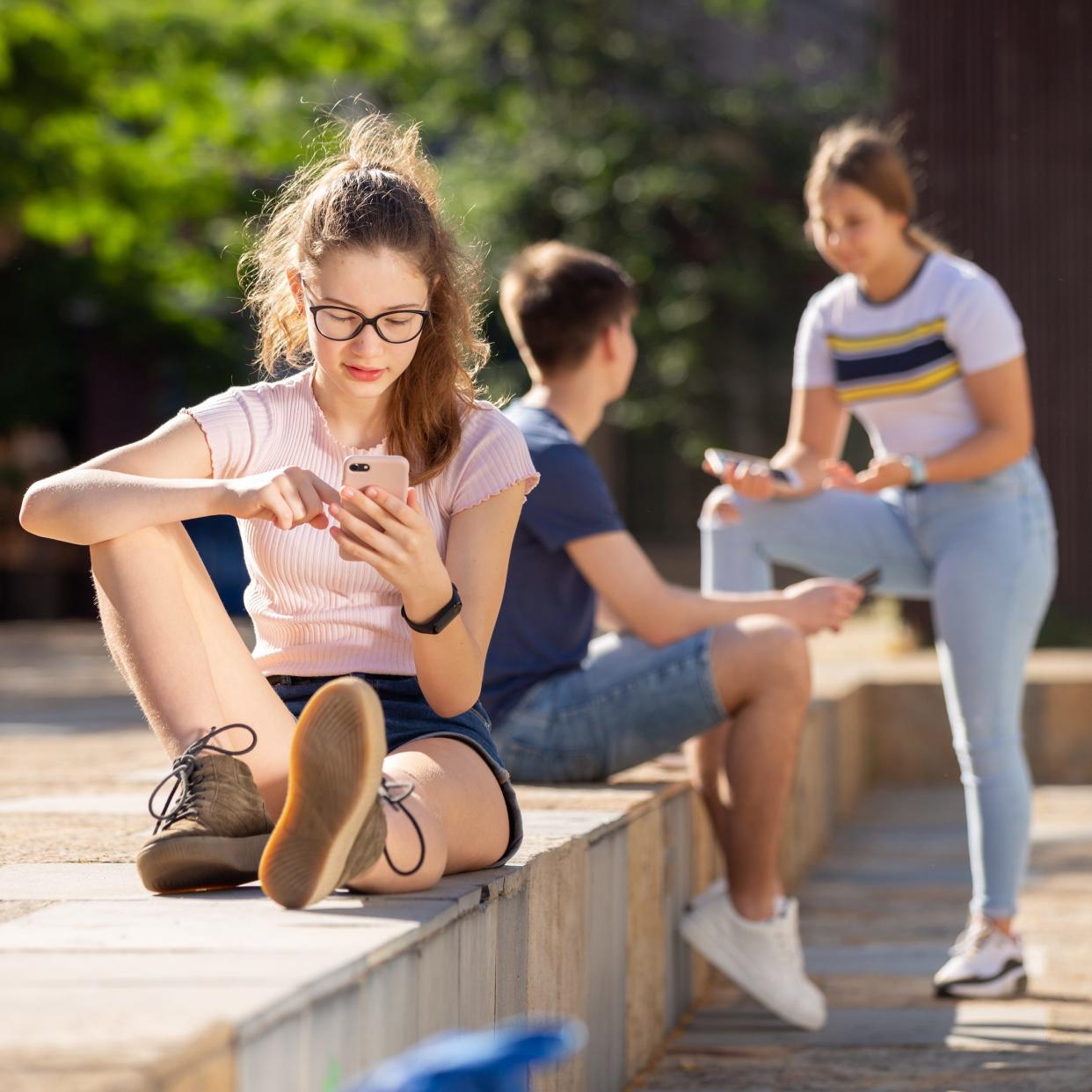 Portrait of teen girl checking her smartphone while outdoors on summer day