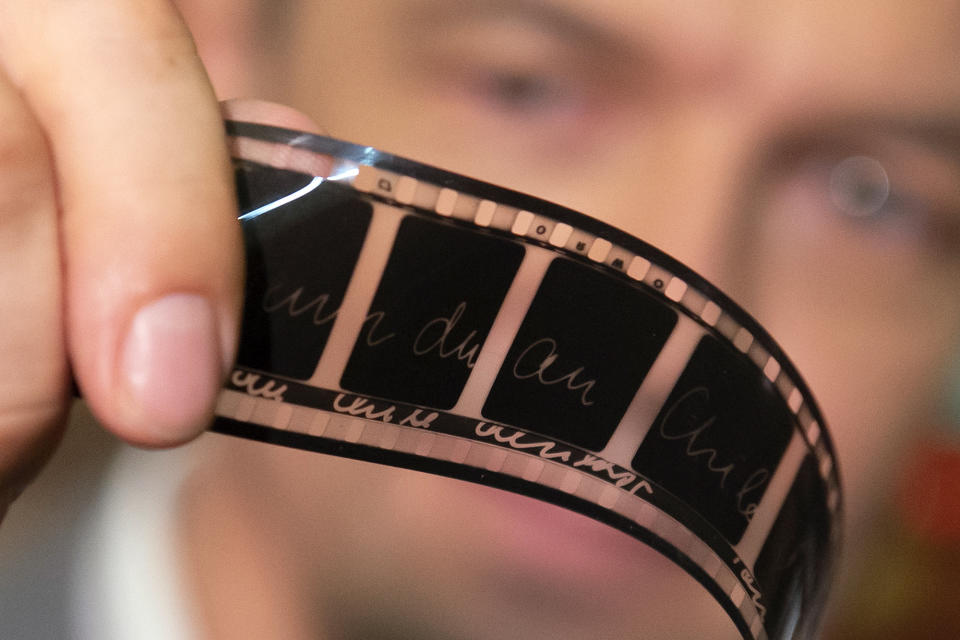 In this Wednesday, June 17, 2020 photo, Gunnar Dedio, German film producer and managing director of PROGRESS Film GmbH looks at a film roll in the archive of PROGRESS Film GmbH in Leipzig, Germany. A new project is underway to digitize thousands of East German newsreels, documentaries and feature films 30 years after Germany’s reunification. The movies that are being scanned, transcribed and posted online provide a look inside a country that no longer exists but was a critical part of the Cold War. (AP Photo/Jens Meyer)