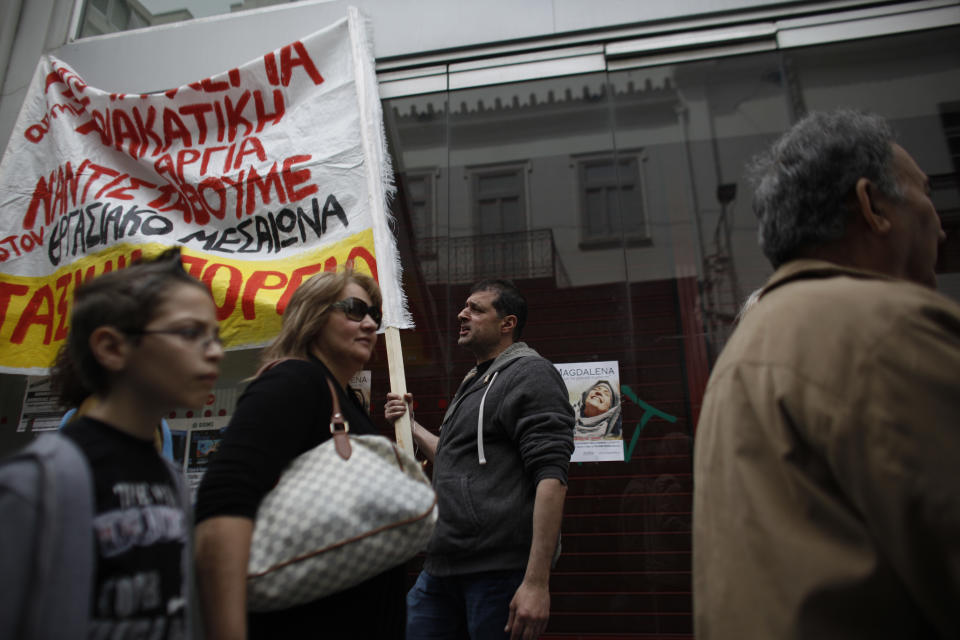 A protester shouts slogans as pedestrians walk in front of a closed shop with a banner that reads "Resist Against the medieval working conditions" during a protest against the opening of shops on Sundays and the extension of working hours, in Athens' Ermou shopping street, on Sunday, April 13 2014. Fitch ratings agency warned the successful bond issue didn't mean an end to Greece's financial problems. In a report Friday it said the issue showed the country's progress but doesn't mean it will be able to finance itself on its own when the bailout program ends later this year. (AP Photo/Kostas Tsironis)