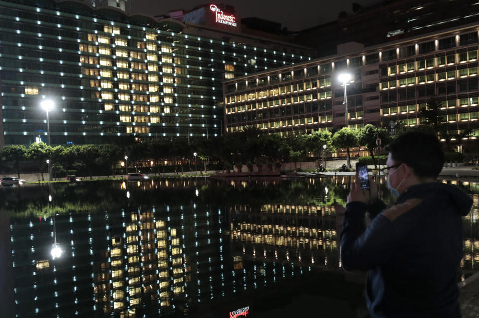 A man uses his mobile phone to take photos of Hotel Indonesia Kempinski, where room lights make the shape of a heart to honor healthcare and other essential workers still on the job, during the new coronavirus outbreak in Jakarta, Indonesia, Friday, April 17, 2020. Indonesia's capital kicked off a stricter restriction to slow the spread of the new coronavirus last week as the metropolitan area has become Indonesia's coronavirus epicenter. (AP Photo/Dita Alangkara)