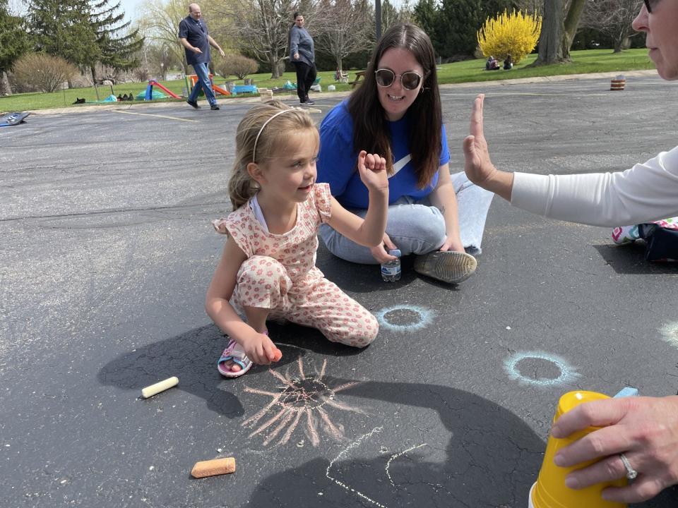 Oakleigh Daniels, 4, high-fives Stephanie Wintersteen, lead youth service technician at Ellis, after creating a chalk project at Monday's eclipse party. Oakleigh's mom, Brooke Daniels, looks on.