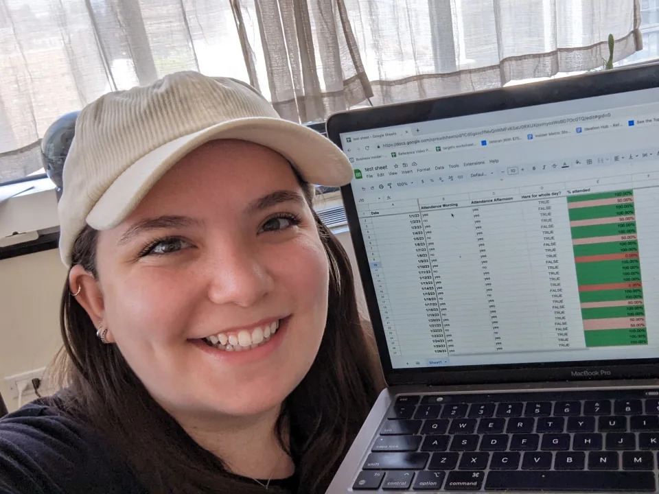 Author of story smiling at camera next to laptop with a spreadsheet on display