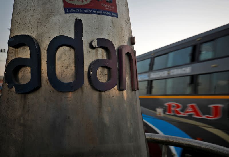 A passenger bus moves past the logo of the Adani Group installed at a roundabout on the ring road in Ahmedabad