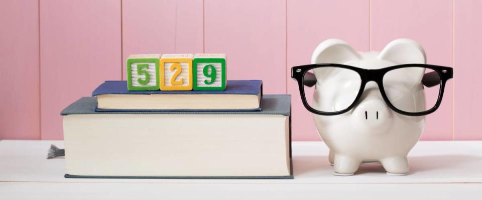 529 in alphabet blocks sit on top of textbooks next to piggy bank wearing eyeglasses