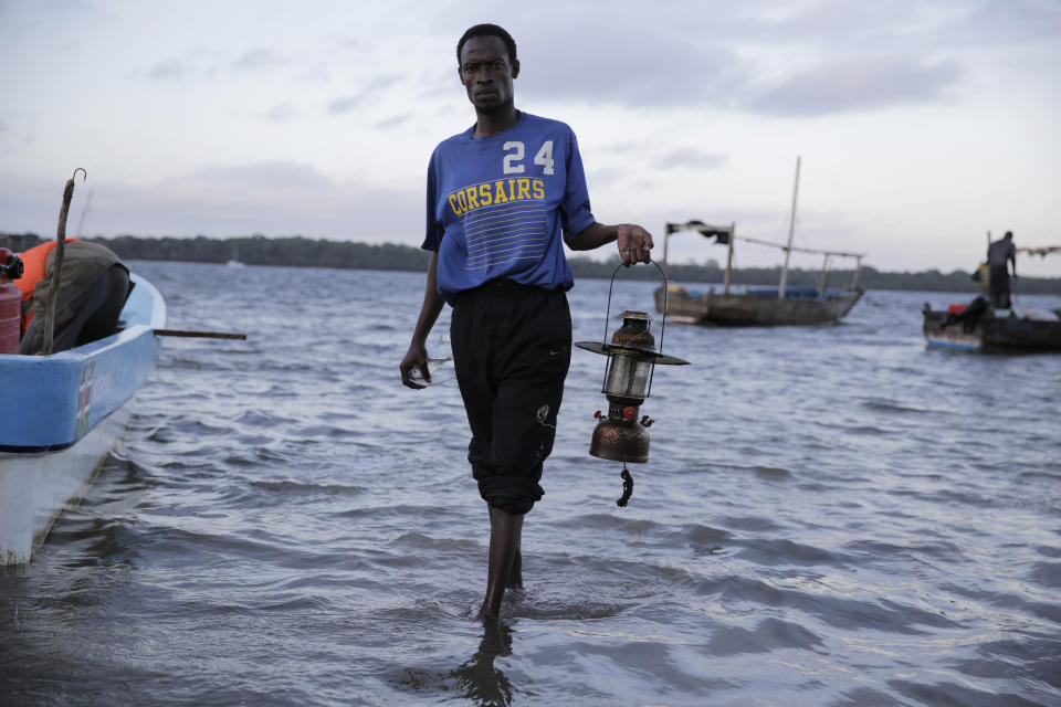 A fisherman comes out of the sea holding his hurricane lantern after a long night of fishing in the Shimoni Fishers Jetty, in Kwale County, Kenya, on Saturday, June 11, 2022. Artisanal fisheries on Kenya's coast say climate change, overfishing by large foreign vessels and a lack of other job opportunities for coastal communities is draining the Indian Ocean of its yellowfin tuna stocks. (AP Photo/Brian Inganga)
