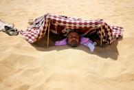 A patient buried in the hot sand looks out from under a shade that protects his face from the sun in Siwa, Egypt, August 12, 2015. (REUTERS/Asmaa Waguih)