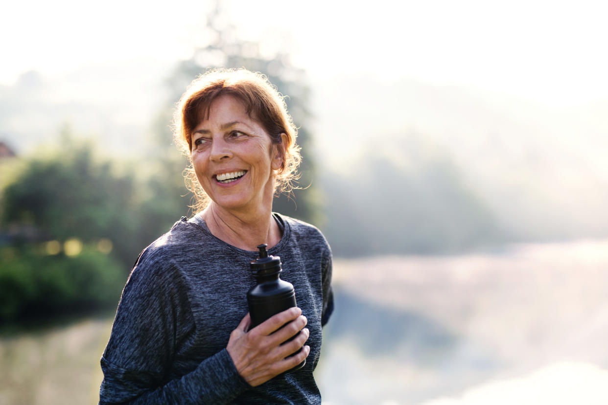 An old female sportsperson with black plastic water bottle doing sport outside in the countryside.