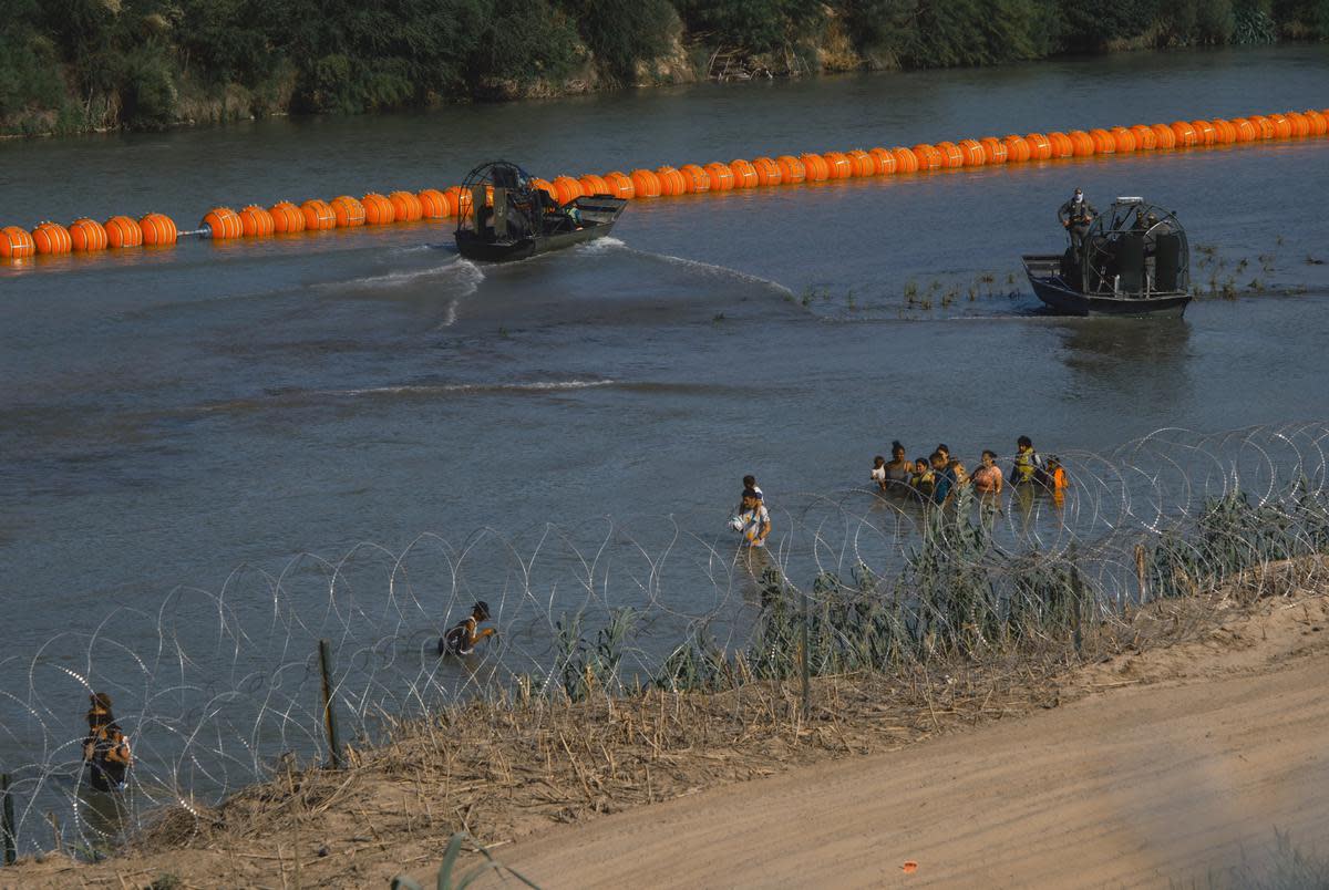 A group of migrants walks around a string of buoys which was deployed to prevent migrants from swimming across the Rio Grande in Eagle Pass on July 14, 2023.