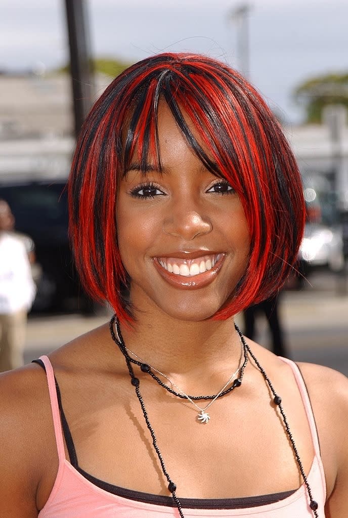 Person with red-streaked bob haircut and light top smiling at the camera