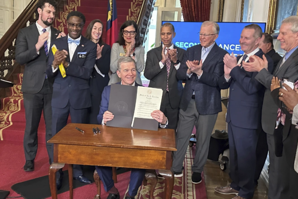 Gov. Roy Cooper holds up a document as those around him applaud