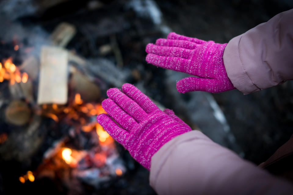 Hands in gloves warming over campfire.