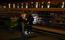 FILE - Customers use the light from a cell phone to look in the meat section of a grocery store Tuesday, Feb. 16, 2021, in Dallas. Even though the store lost power, it was open for cash only sales. A series of winter storms and widespread power outages gripping Texas and other states not used to such extreme low temperatures are creating big challenges in the nation’s food supply networks.(AP Photo/LM Otero)