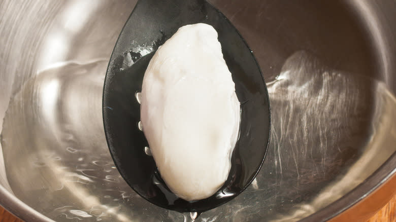 poached egg in spoon over bowl of water