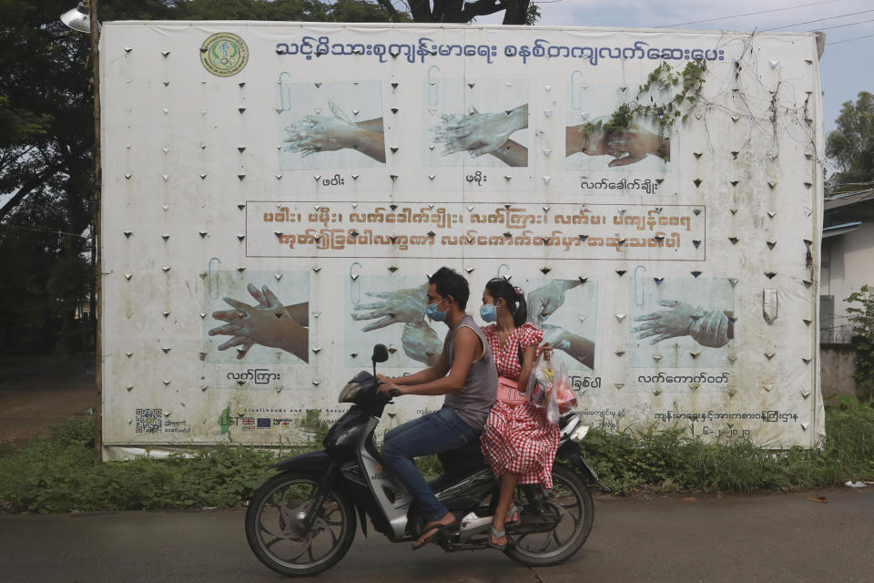 People wearing face masks to help curb the spread of the coronavirus ride a motorcycle past a Health Ministry public information campaign billboard about proper hand washing in Shwe Pyi Thar township in Yangon, Myanmar Wednesday, July 28, 2021. (AP Photo)