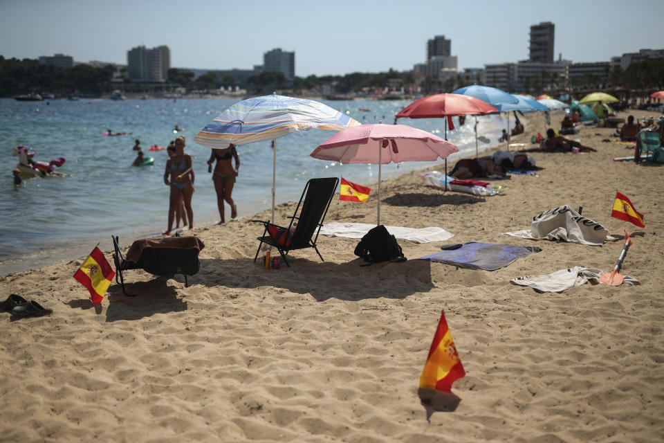 Spanish flags being used as social distancing signage stick out from the sand in Palma de Mallorca, Spain, Sunday, July 26, 2020. Britain has put Spain back on its unsafe list and announced Saturday that travelers arriving in the U.K. from Spain must now quarantine for 14 days. The move by the UK taken without forewarning has caught travelers off guard. (AP Photo/Joan Mateu)