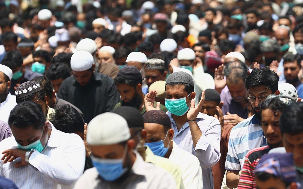 Muslims wear face masks as they participate in Friday prayers on a road side in Karachi - Shutterstock