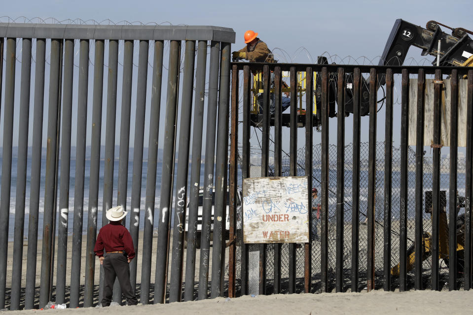 Un hombre en el lado estadounidense de la frontera (arriba) trabaja en la estructura ante la mirada de otro desde la playa, en Tijuana, México, el 15 de noviembre de 2018. (AP Foto/Gregory Bull)