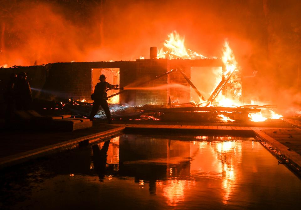 In this Nov. 9, 2018 file photo, a firefighter battles the Woolsey Fire burning a home in Malibu.