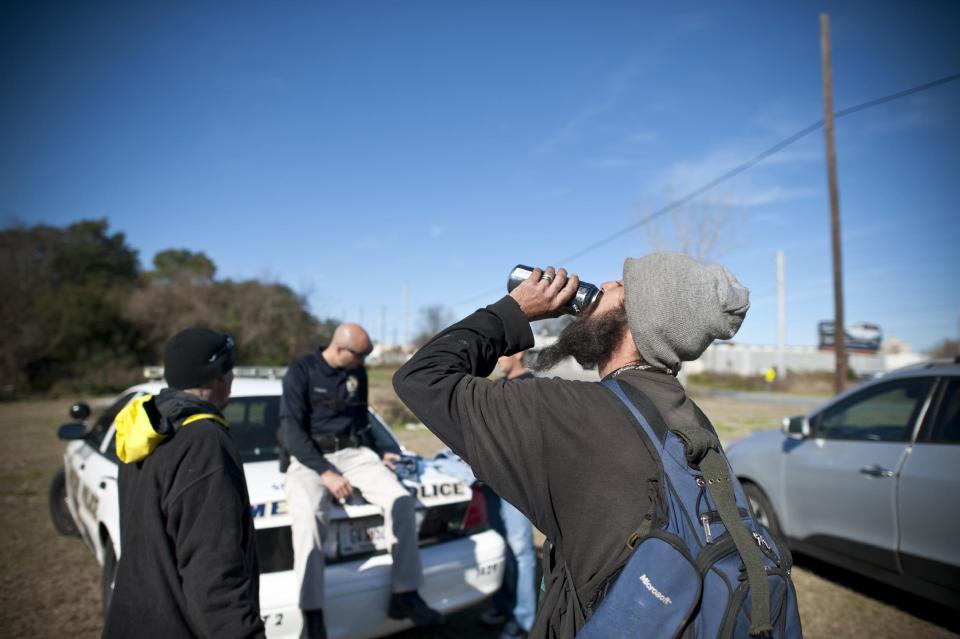 In this Thursday, Dec. 19, 2013 photo, a homeless man takes a quick swig of beer that was hidden in his sleeve while Homeless Liaison Officer Tom Gentner, center, meets with a group of volunteers in Savannah, Ga. Gentner uses a balance of tolerance and enforcement to keep the peace and earn the trust of the over 300 people living in the 20 homeless camps around the Historic District. (AP Photo/Stephen B. Morton)