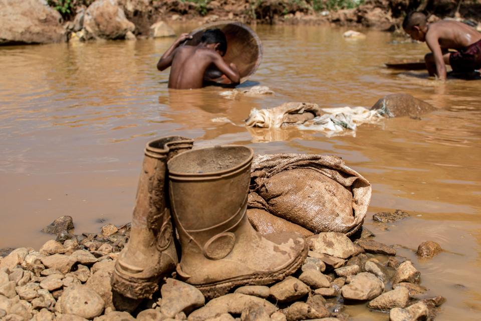 A pair of boots and other tools used in an open pit mine are seen as Venezuelan children work through the mud in search of gold in El Callao, Bolivar State, Venezuela, in a Sept. 2, 2023. / Credit: YRIS PAUL/AFP/Getty