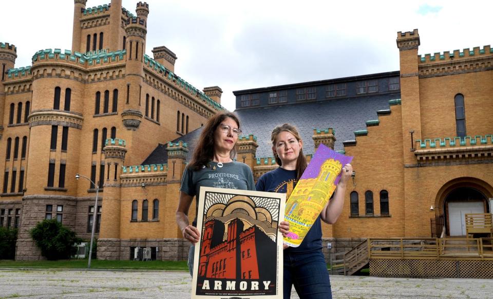 With the Cranston Street Armory in the background, Kari Lang, left, former head of the West Broadway Neighborhood Association, holds a 2007 poster by Peter Cardoso, and WBNA board chair Rebecca Atwood holds a 2013 artwork by Walker Mettling promoting the building's reuse.