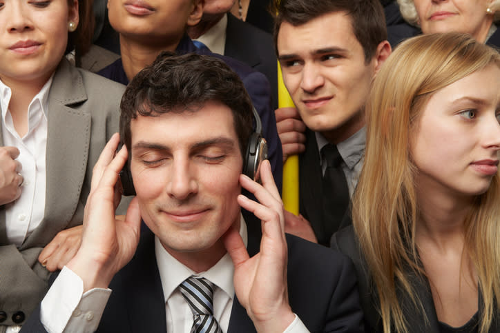 A man in a suit listening to his headphones on a crowded train.